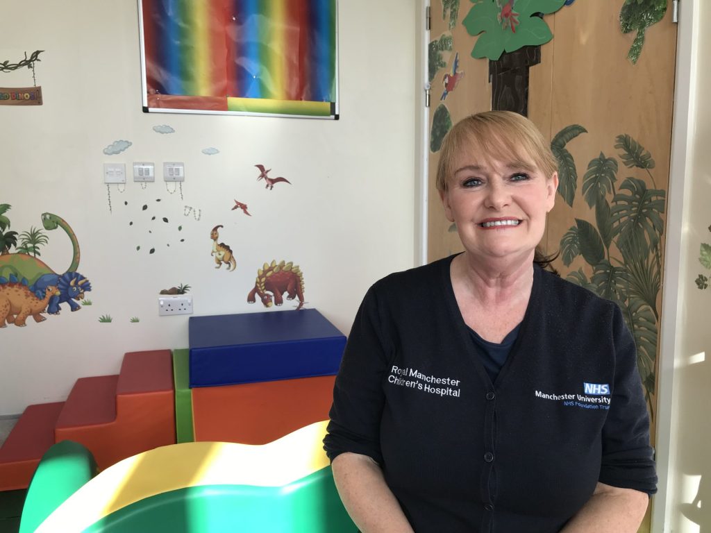 Susan Fairclough in play leader uniform sits in colourful playroom