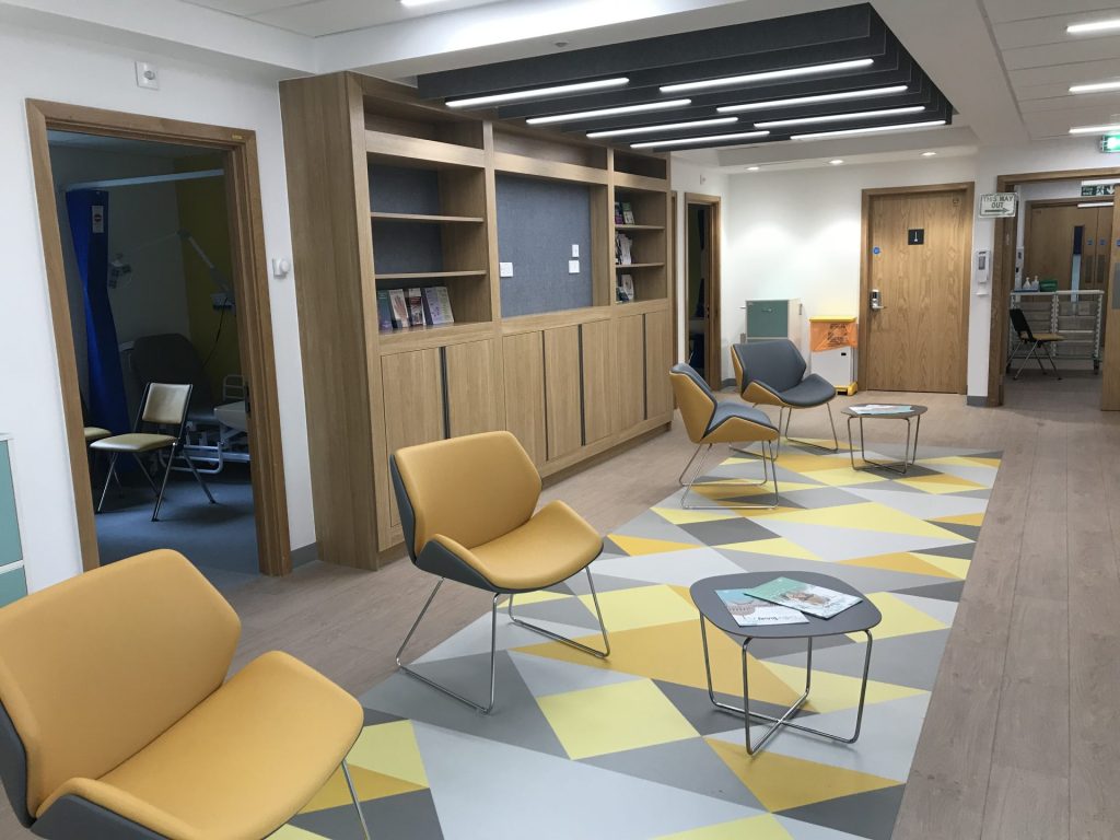 Waiting room in hospital with yellow and grey flooring and chairs.