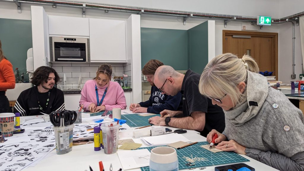 A group of staff members sit around a table doing lino cutting arts and crafts