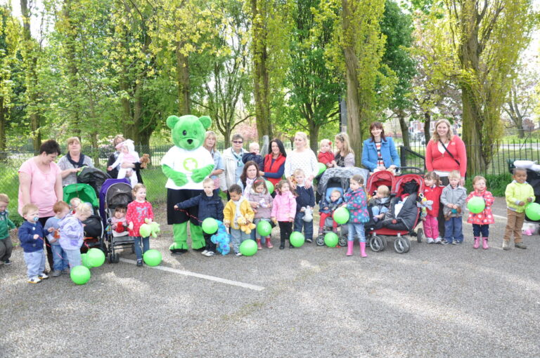 Large group of adults and children standing near trees with Humphrey Bear